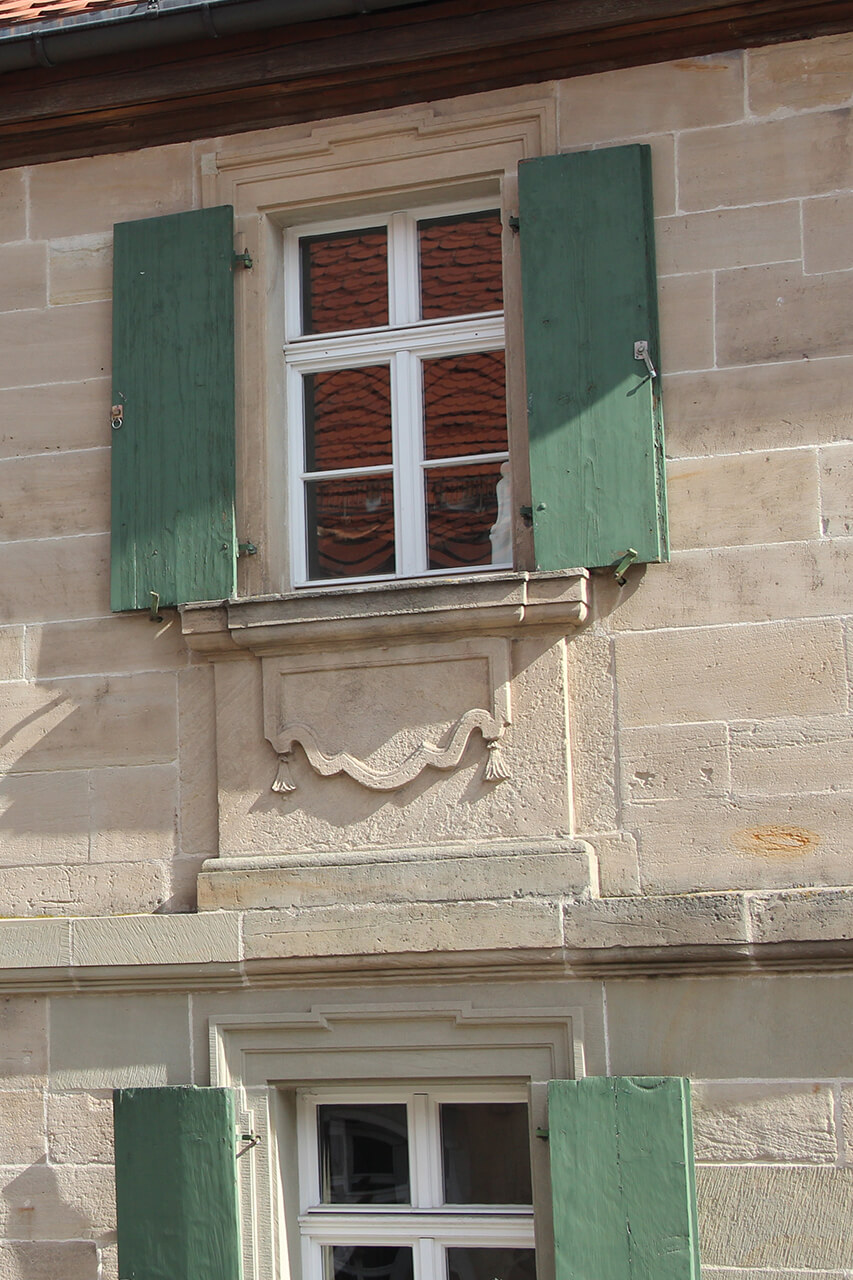 Ebenfalls einfach gehaltene Fensterschürzen (1776), ohne seitliche Tri- oder Diglyphen. Die Fensterschürze zeigt jedoch bereits eine ausgeprägte Plastizität, u.a. durch die Vertiefung des inneren Schürzenfeldes und filigraner herausgearbeitete Quasten (Weidenberg, Oberer Markt).